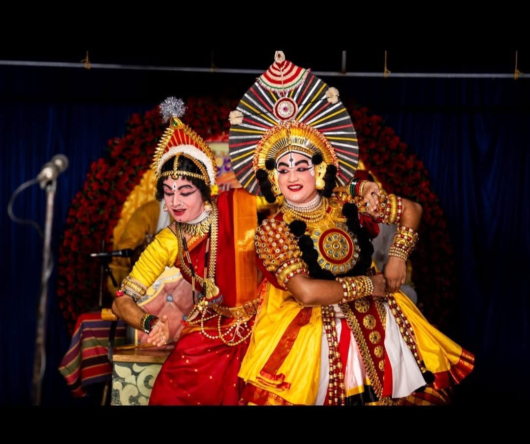 Two female performers in colourful striped costumes and large head-dresses