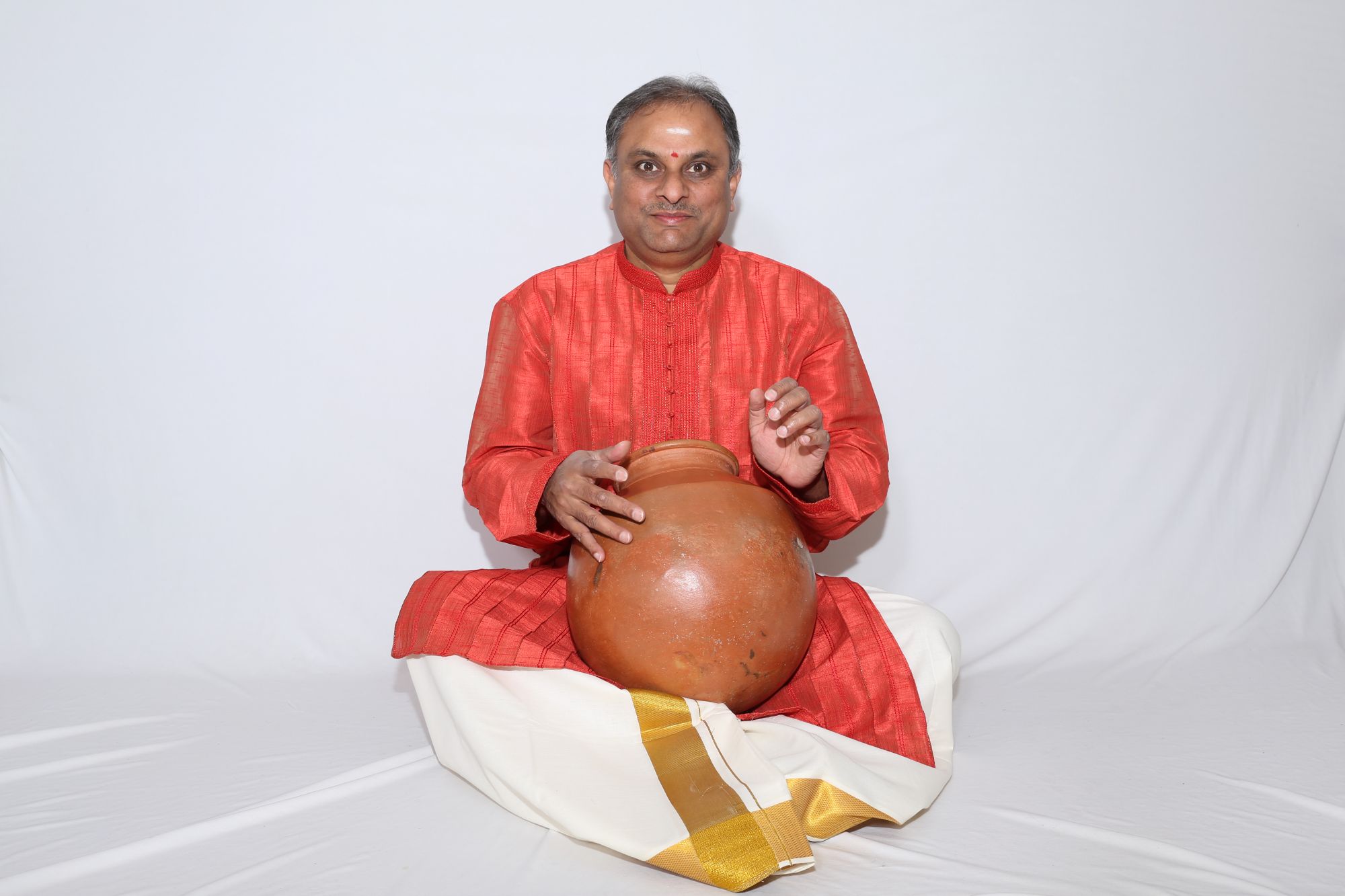 RN Prakash, seated with a drum in his lap, wearing red and white, looks at the camera