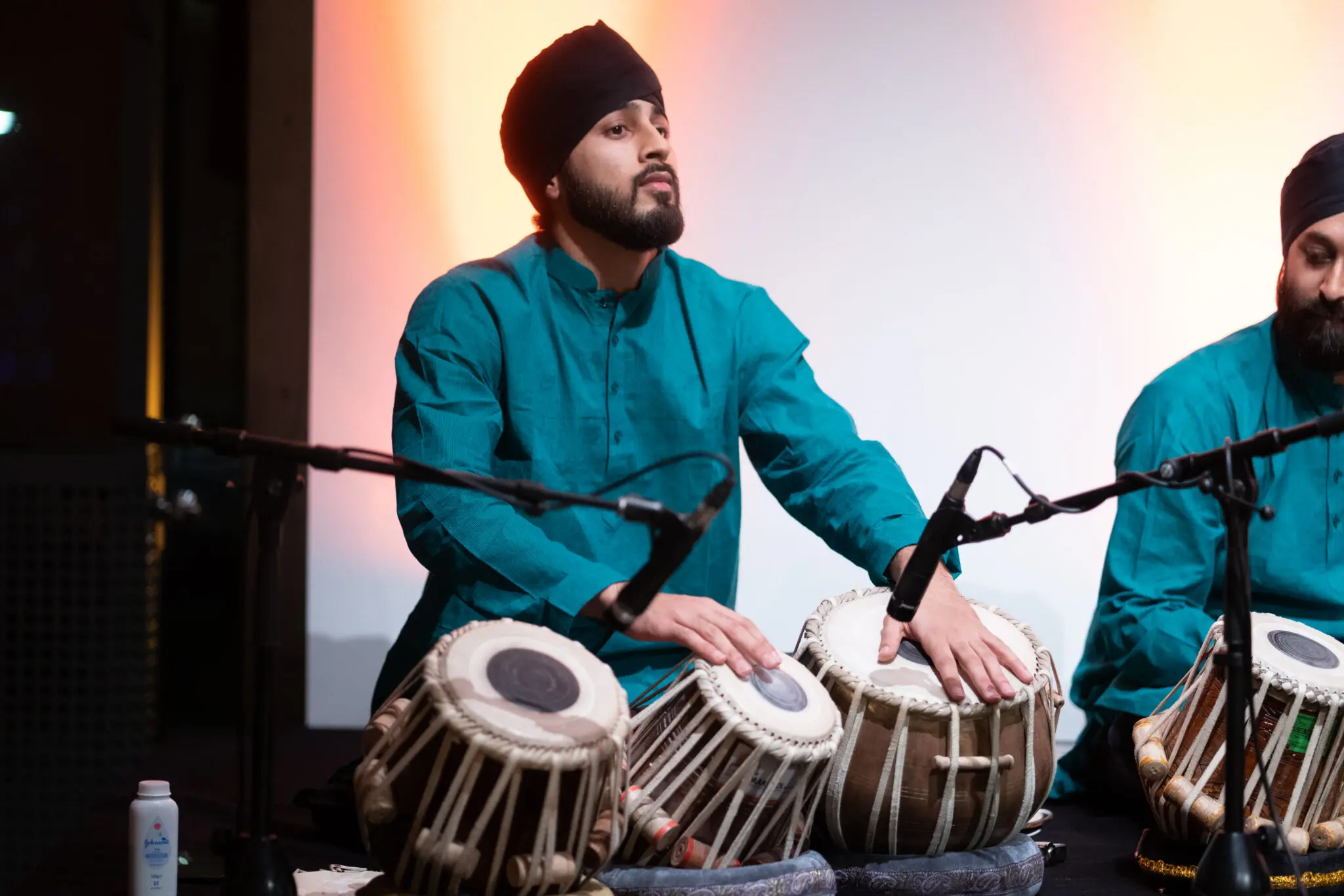 Harkiret Singh Bahra stands on stage playing an array of tabla in front of him