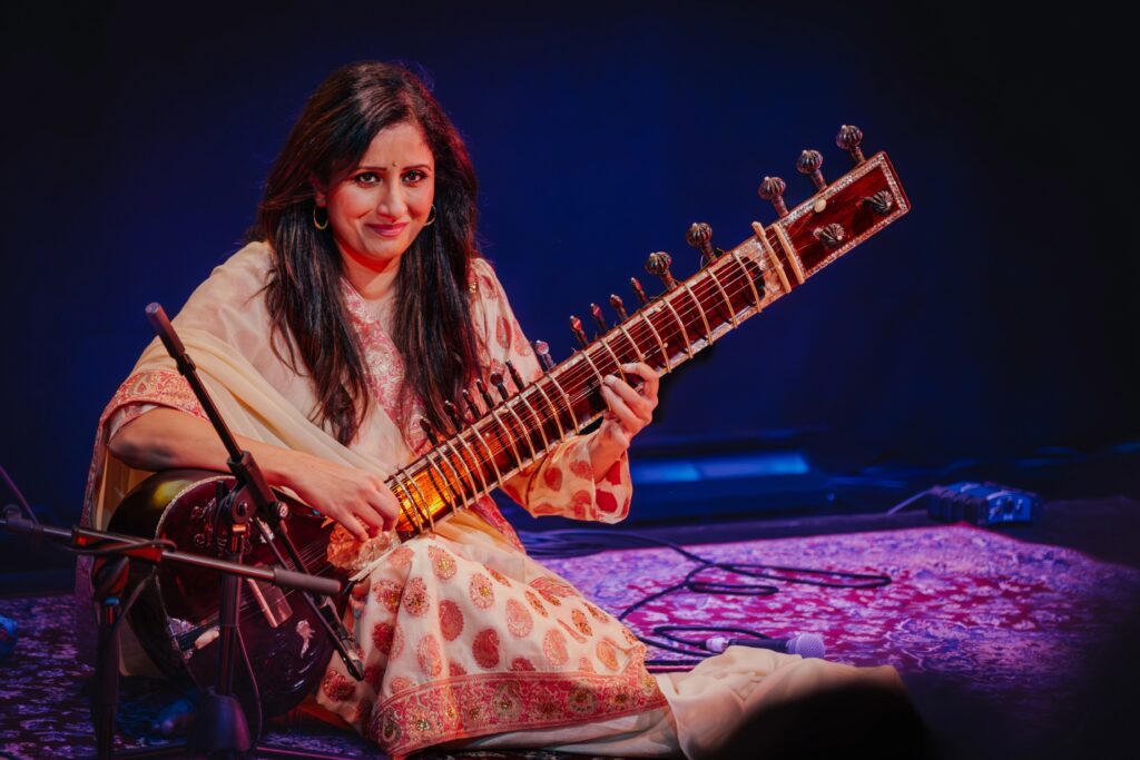 Roopa Panesar, seated on stage, with her sitar on her lap