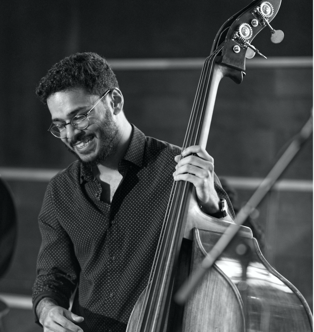 Black and white shot of Shivraj Singh, stood with his double-bass and smiling